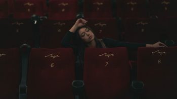 A woman in black long sleeves sitting in an empty theater, surrounded by red seats.